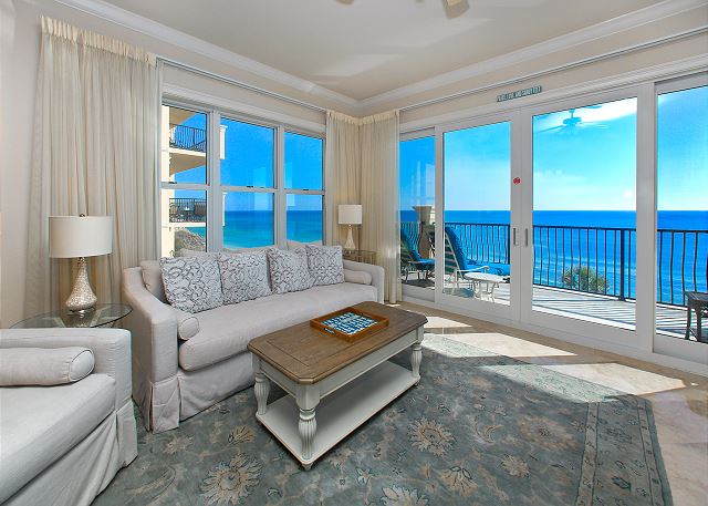 View of the living room with white, modern furniture - balcony in the backdrop overlooking the ocean