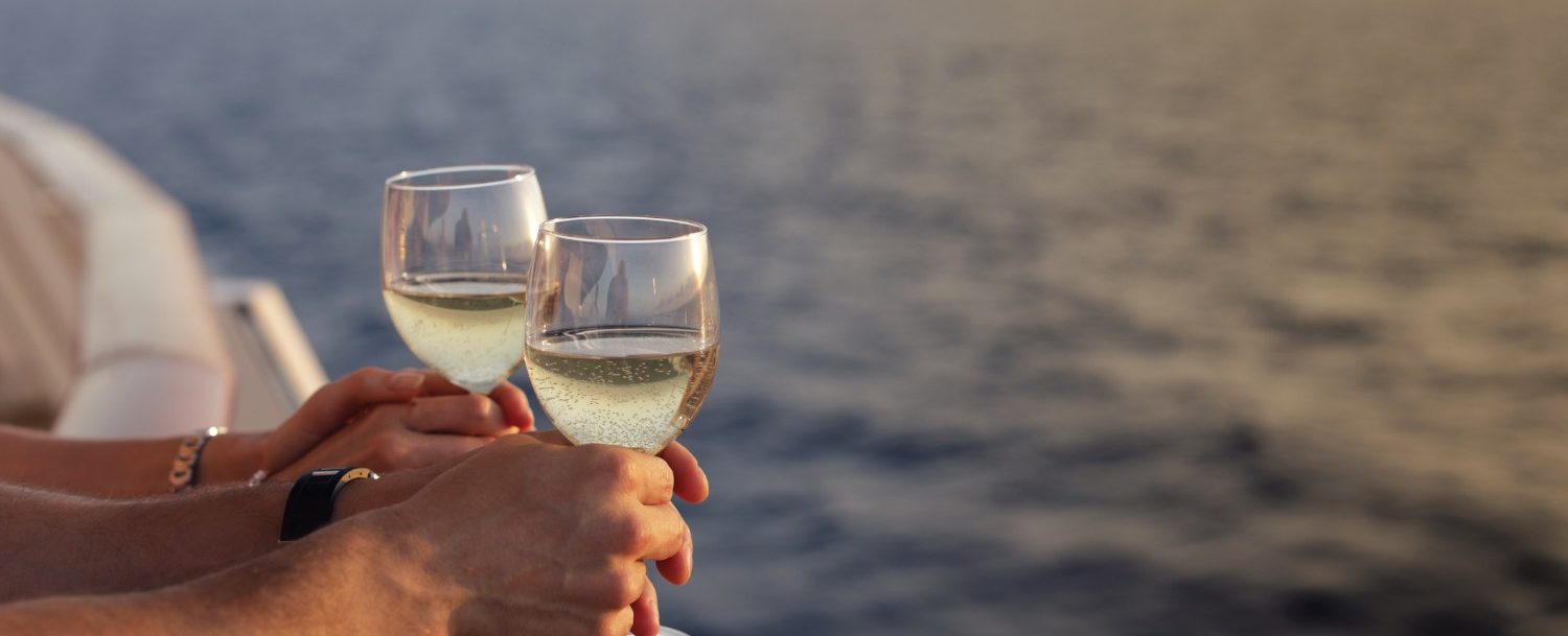 Close up of couple's hands on a sunset cruise with drinks with ocean in the background