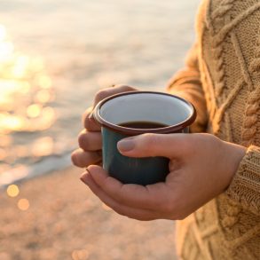 Woman holding a cup of coffee on the beach in October in Destin