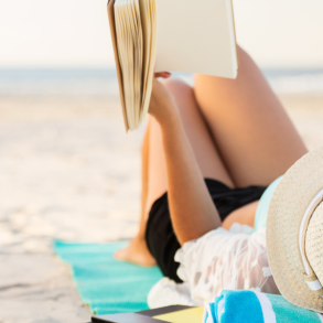 woman laying on beach reading a book
