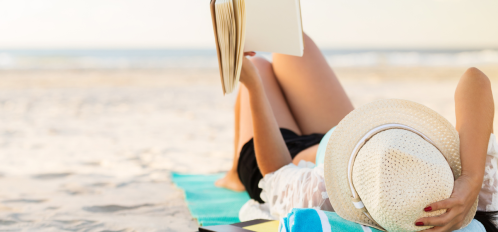 woman laying on beach reading a book