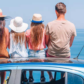 family of four sitting on car overlooking water