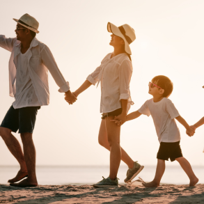 family of four holding hands and walking away from car on beach