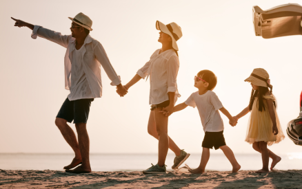 family of four holding hands and walking away from car on beach
