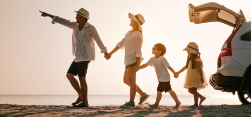 family of four holding hands and walking away from car on beach