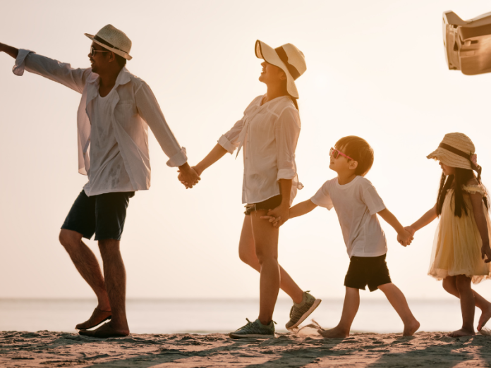 family of four holding hands and walking away from car on beach