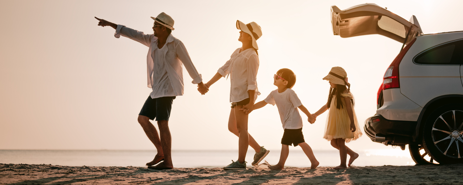family of four holding hands and walking away from car on beach