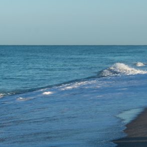 Retired couple walk along Florida beach at sunrise.