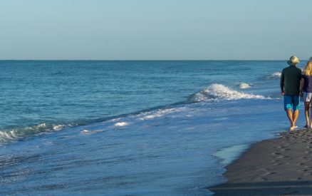 Retired couple walk along Florida beach at sunrise.