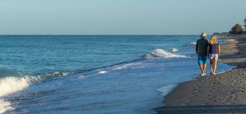 Retired couple walk along Florida beach at sunrise.