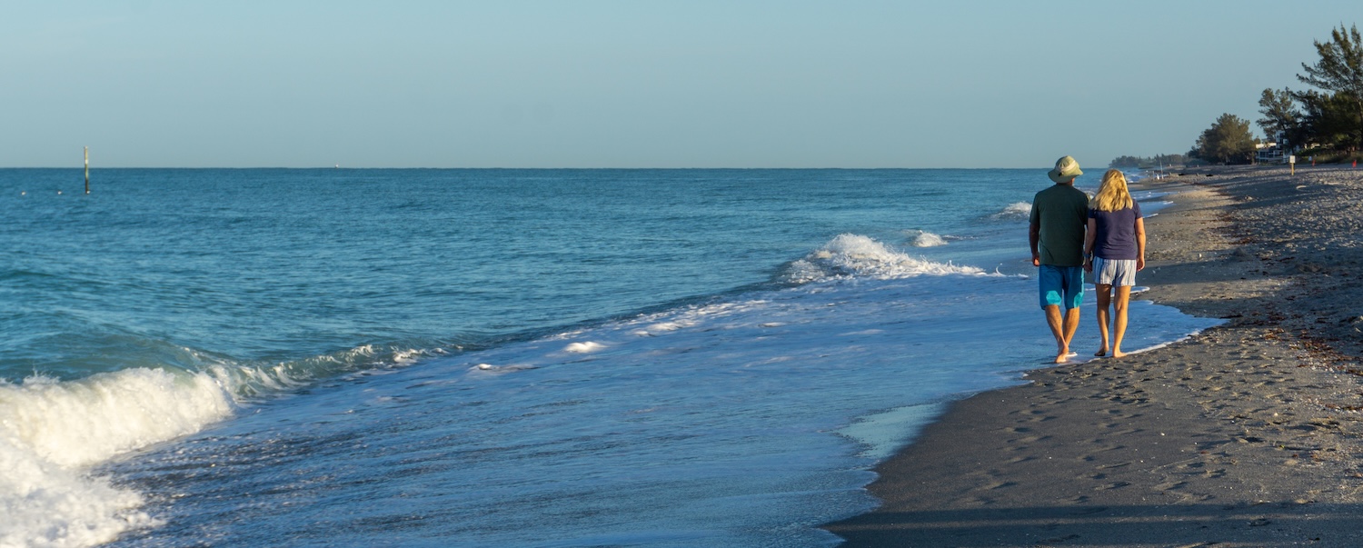 Retired couple walk along Florida beach at sunrise.